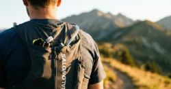 Detail běžeckého batohu na zádech běžce na horské stezce.