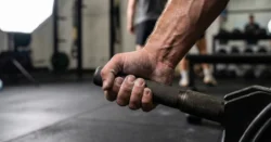 Detail ruky sportovce pevně svírající činku v posilovně.