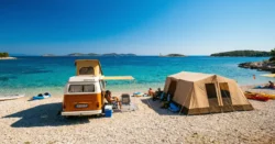 Stylový karavan nebo velký rodinný stan postavený přímo na oblázkové pláži v Chorvatsku s tyrkysovou vodou a ostrovy.