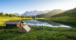 Útulný stan nebo malá dřevěná chata u klidného alpského jezera v Rakousku, obklopená zasněženými horami.