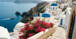 Ikonické bílé domy s modrými kopulemi na řeckém ostrově s výhledem na Egejské moře a kvetoucí bugenvileu.