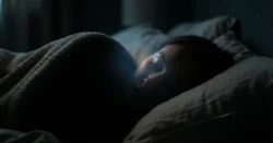 Atmosférická fotografie osoby spící v temné, klidné ložnici s jemným světlem.