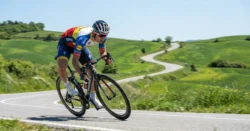 Silniční cyklista v zatáčce na klikaté cestě v kopcovité krajině.