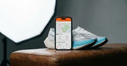 Detail chytrého telefonu s aplikací pro sledování fitness aktivit vedle běžeckých bot.